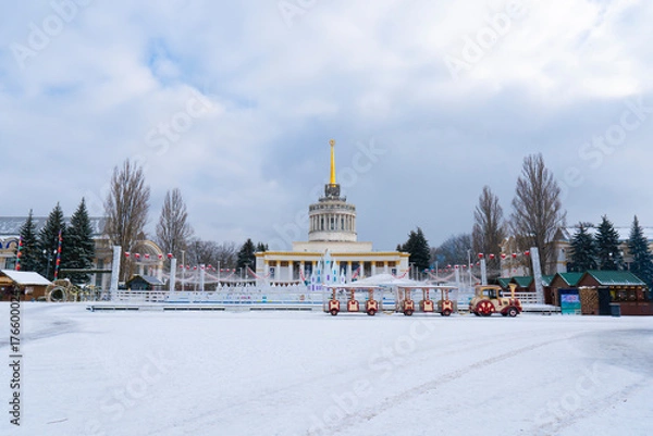 Fototapeta Beautiful wide shot of the central VDNKh (Expocenter of Ukraine) pavilion in Kyiv on a snowy winter day, showing the decorated ice rink
