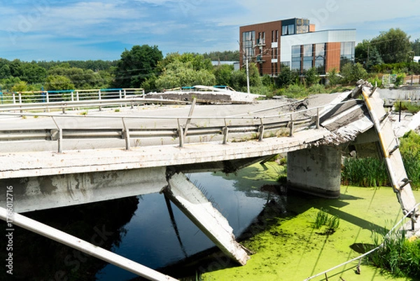 Fototapeta A concrete road bridge, destroyed as a result of hostilities, collapses over a ditch of stagnant green water, symbolizing the devastating impact of war