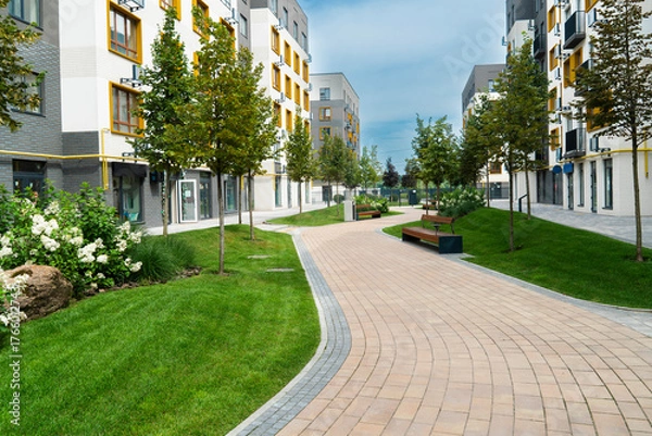 Fototapeta A curving paved path through the green lawn and young trees of a well-landscaped courtyard in a modern residential apartment block complex