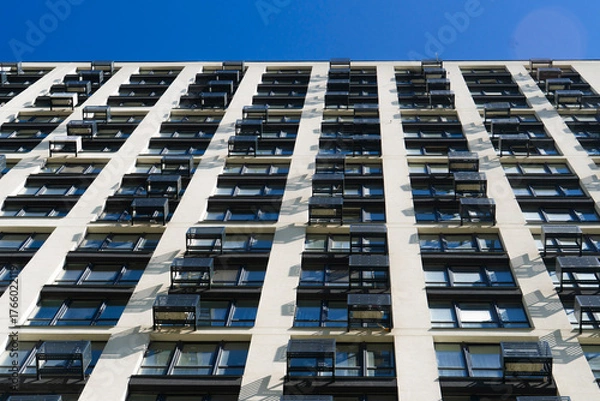 Fototapeta Abstract low-angle view of a modern high-rise residential building facade with repetitive rows of windows and white walls under a clear blue sky