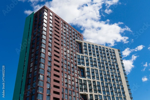 Fototapeta Striking architectural detail of a contemporary high-rise apartment building with contrasting colored facades set against a dramatic, cloudy blue sky