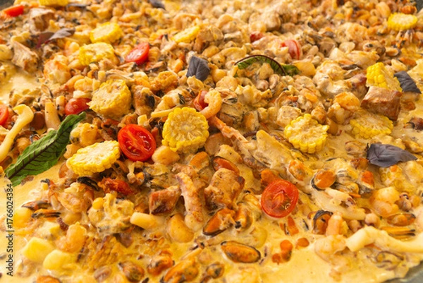 Fototapeta Full-frame close-up of a rich, creamy paella dish filled with mussels, shrimp, corn, and cherry tomatoes, cooked in a rich yellow sauce