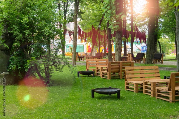 Fototapeta Cozy outdoor lounge and dining area in a green park with handmade rustic wooden pallet furniture and fire pits under the canopy of trees