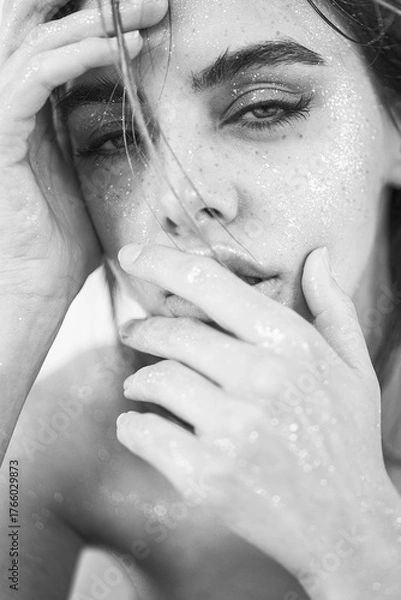 Fototapeta Studio close-up of a beautiful woman with natural makeup, wet hair, and sparkling glitter on her skin. 