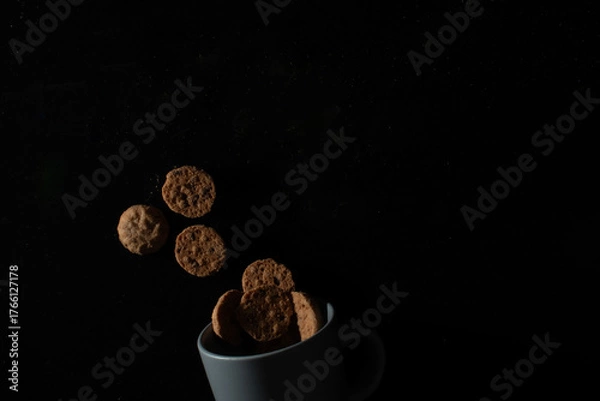 Obraz Cookies floating above a cup on dark background