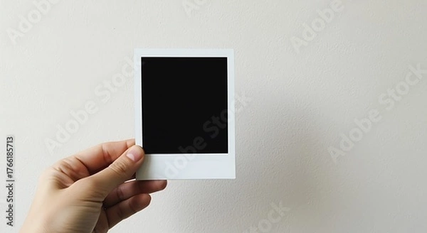 Fototapeta Hand holding blank black instant photo frame against textured wall polaroid