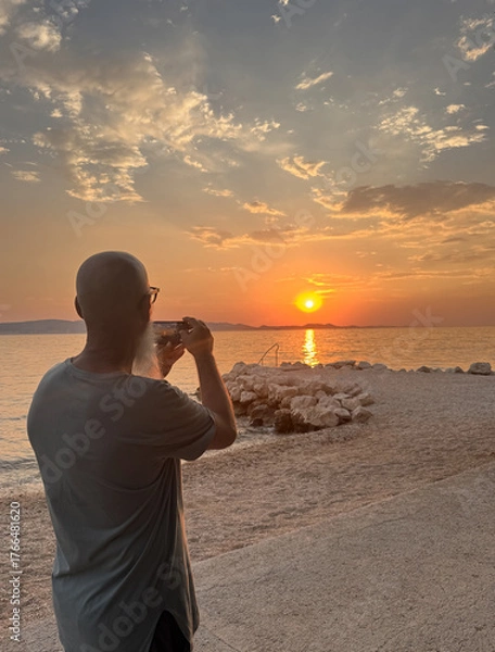 Obraz rear view of man with beard standing alone on the beach taking photo of sunset sky over Adriatic Sea in Dalmatia, Croatia