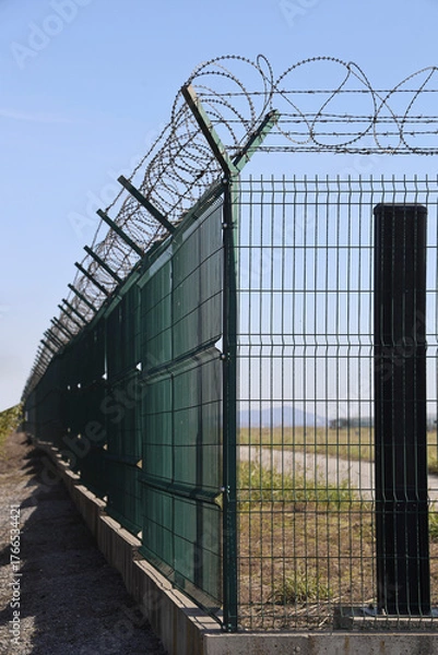 Obraz metal grid fence with barbed wire against the blue sky Border of runway