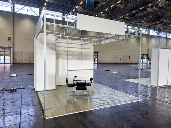Fototapeta Weisser leerer Messestand in Messehalle mit schwarzen Stühlen und einem Tisch
