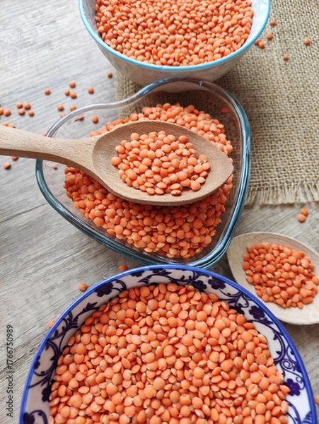 Fototapeta Dried small red lentils in a decorative plate and wooden spoons on a wooden background	