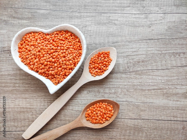 Fototapeta Dried small red lentils in a decorative plate and wooden spoons on a wooden background	