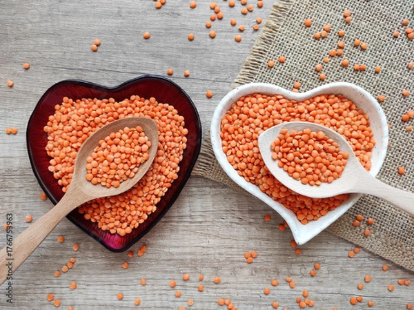 Fototapeta Dried small red lentils in a decorative plate and wooden spoons on a wooden background	