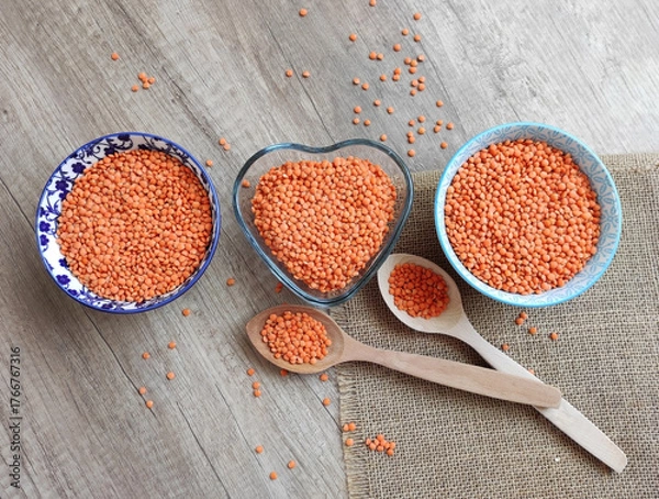 Fototapeta Dried small red lentils in a decorative plate and wooden spoons on a wooden background	