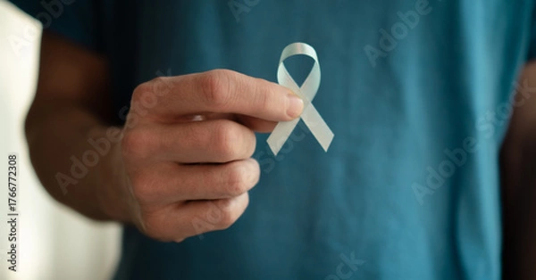 Obraz Close up of a young man holding a blue ribbon in his hand. Symbol of prostate cancer awareness, early diagnosis, medical support, oncology care, and prevention concept.