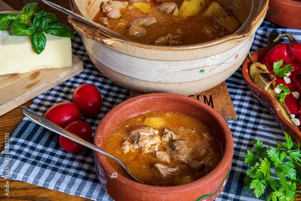 Fototapeta A warm bowl of cooked potato soup placed on a table, showcasing its creamy texture, soft vegetables, and homemade appearance. The natural lighting highlights the comforting and rustic feel of the dish
