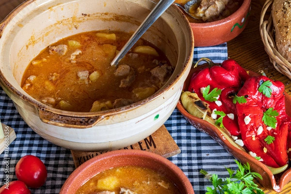 Fototapeta A warm bowl of cooked potato soup placed on a table, showcasing its creamy texture, soft vegetables, and homemade appearance. The natural lighting highlights the comforting and rustic feel of the dish