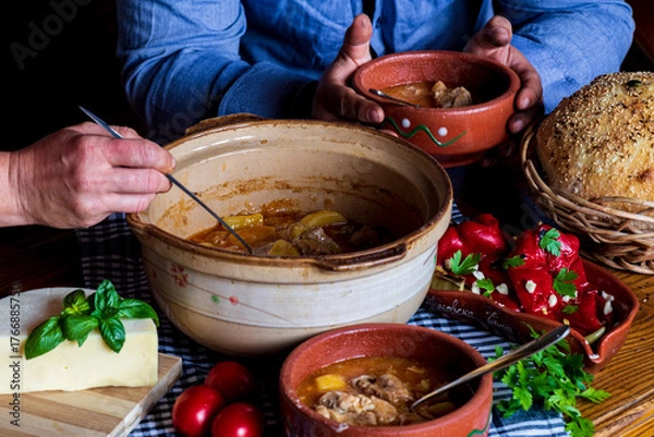 Fototapeta A warm bowl of cooked potato soup placed on a table, showcasing its creamy texture, soft vegetables, and homemade appearance. The natural lighting highlights the comforting and rustic feel of the dish