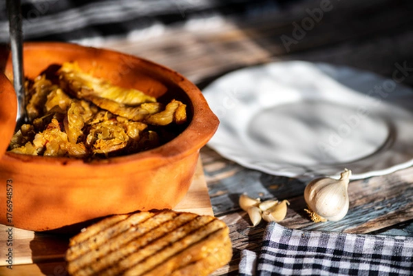 Fototapeta A bowl of cooked cabbage served in a rustic brown dish, showcasing its soft texture and warm, comforting appearance. The natural colors and simple presentation make this image suitable for traditional