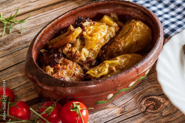 Fototapeta Traditional cabbage rolls (sarma) served in a rustic brown bowl, showcasing tender leaves stuffed with a savory meat and rice filling. The warm, hearty dish is highlighted by natural lighting, emphasi