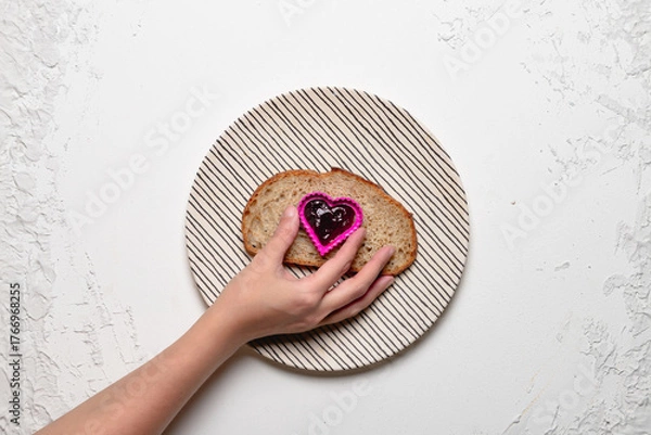 Fototapeta Hand Holding a Heart-Shaped Mold with Jam on Bread Slice