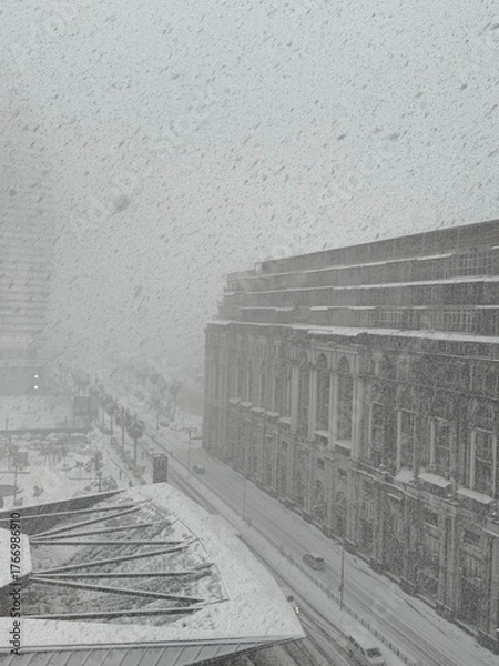 Fototapeta Large building and snowy street with cars and bus during heavy snowfall. Used in architecture, transport, and climate materials.