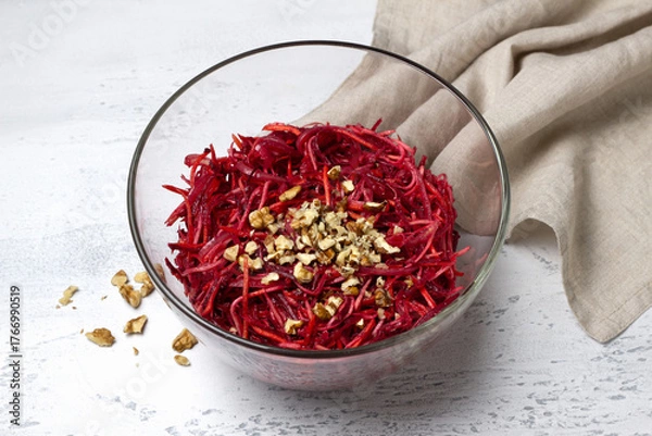 Obraz Healthy beetroot salad with shredded carrot, celery, onion, and chopped walnuts in a glass bowl on light textured background. Fresh vegetarian dish, close-up, with copy space for text or design