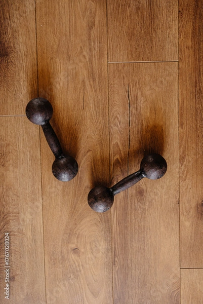 Obraz Two black dumbbells for sports lying on a wooden floor, filmed from above