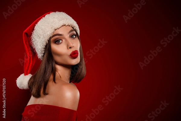 Fototapeta Glamorous Christmas portrait of a stylish woman in a Santa hat with red lipstick in a festive studio setting