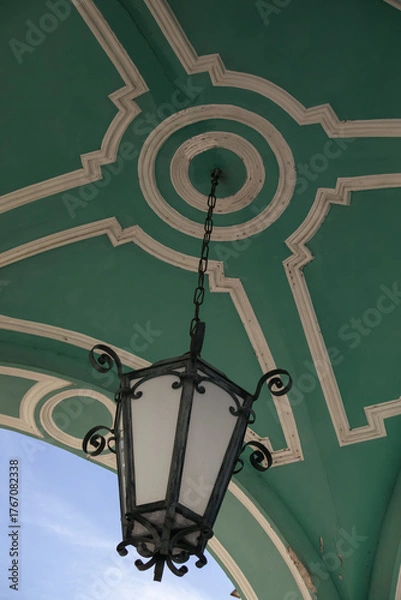 Obraz Close-up of antique lantern hanging on decorative green ceiling with classic architectural molding and blue sky background.