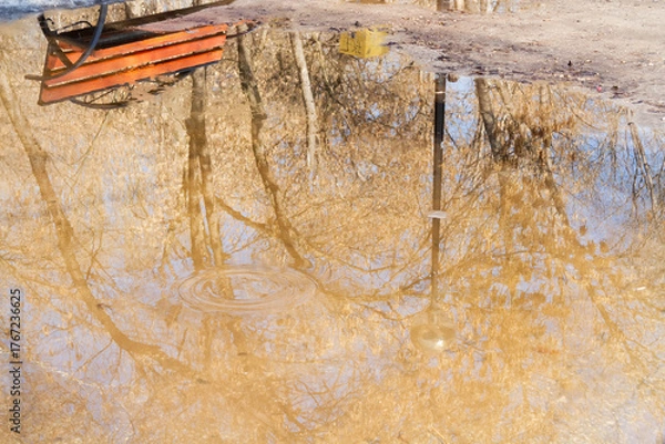 Fototapeta Wooden bench in the spring park. Bright spring sun and snow in the park. Place to rest for a walk. Morning walk..