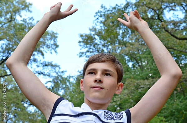 Fototapeta Teenager boy in a white shirt without sleeves with hands outstretched in a gesture of victory 
