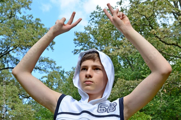 Fototapeta Teenager boy in a white shirt without sleeves with hands outstretched in a gesture of victory
