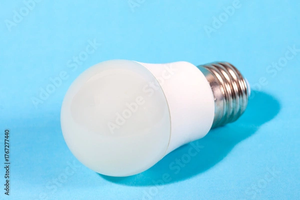 Fototapeta A modern, white LED light bulb isolated against a plain light blue background. A concept for ideas, innovation, illumination, energy saving, and technology.