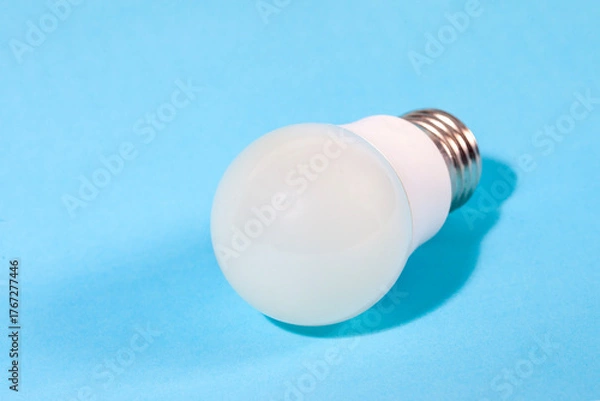 Fototapeta A modern, white LED light bulb isolated against a plain light blue background. A concept for ideas, innovation, illumination, energy saving, and technology.