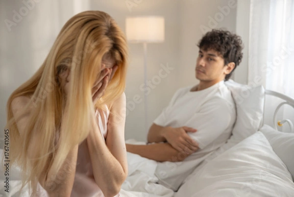 Fototapeta Sad women covering her face while man sits in background with arms crossed. Concept of relationship conflict, emotional stress, couple fight, heartbreak, breakup, sadness and communication issues.