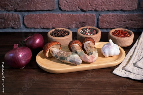 Obraz Wild mushrooms Leccinum aurantiacum on wooden plate with garlic, red onions and spices on rustic table