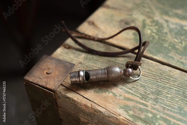 Fototapeta An antique alarm whistle lies on a wooden table.A whistle for giving a signal with a leather cord.