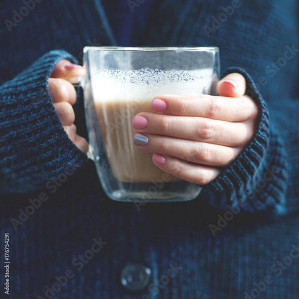 Fototapeta Female hand with a delicate pink manicure holds a transparent mug with double glass with coffee in hands. concept autumn