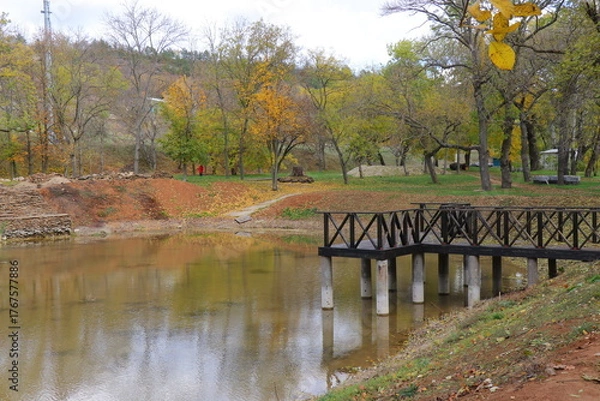 Fototapeta Beautiful autumn park filled with golden-yellow trees, cozy benches, and winding walking paths. Fallen leaves cover the ground, creating a peaceful and romantic atmosphere perfect for relaxation