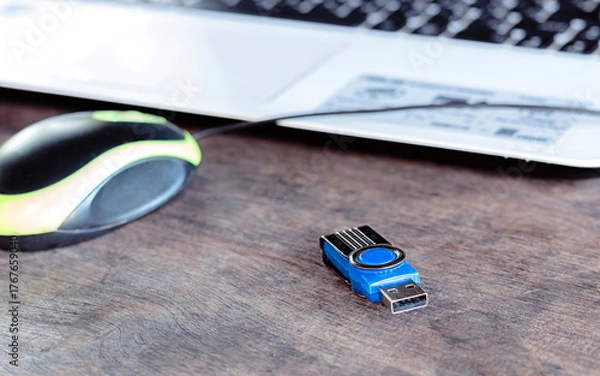 Fototapeta Close-up of USB flash drive, mouse, and laptop keyboard on wooden desk—everyday tech tools in a casual workspace.