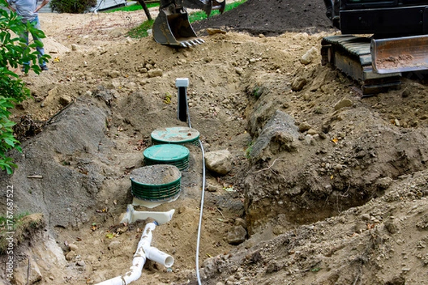Fototapeta Partially buried treatment tank and UV disinfector with pipe connected, and the drain field in the background at a home septic system installation