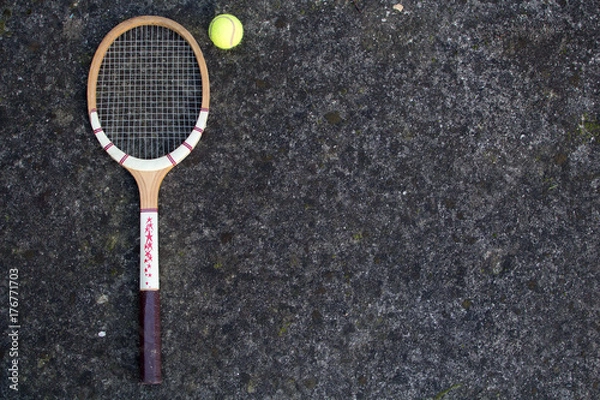 Fototapeta Old vintage wooden tennis racket on isolated stone background with green ball.