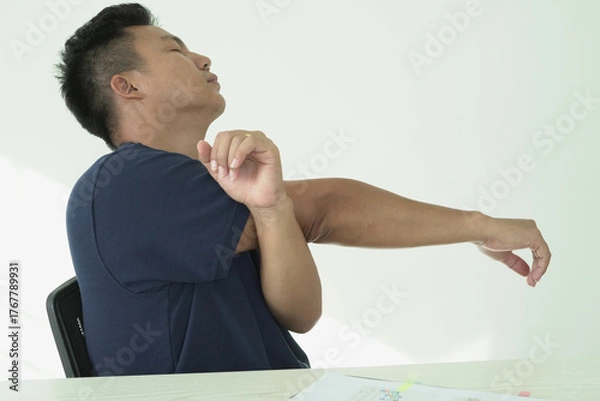 Fototapeta Young asian businessman is suffering pain on wrist, finger and arm, arthritis inflammation while working and he is massaging himself and doing exercise with his hands to relax and to relieve pain.
