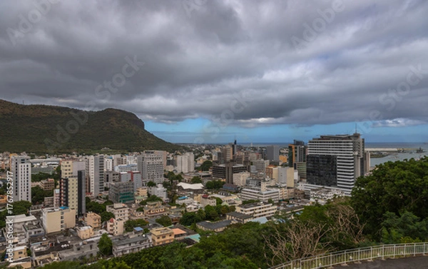 Fototapeta Panoramic view of Port Louis, the capital city of Mauritius, with a dramatic mountain range in the background under moody skies. This urban landscape highlights the contrast 