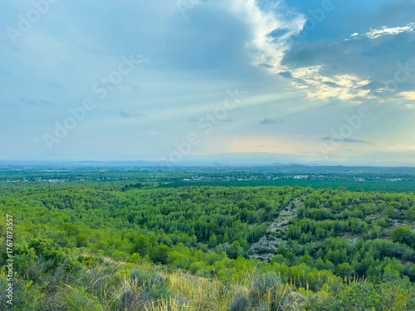 Fototapeta Expansive green landscape under a cloudy sky with rays of sunlight breaking through in a peaceful rural setting