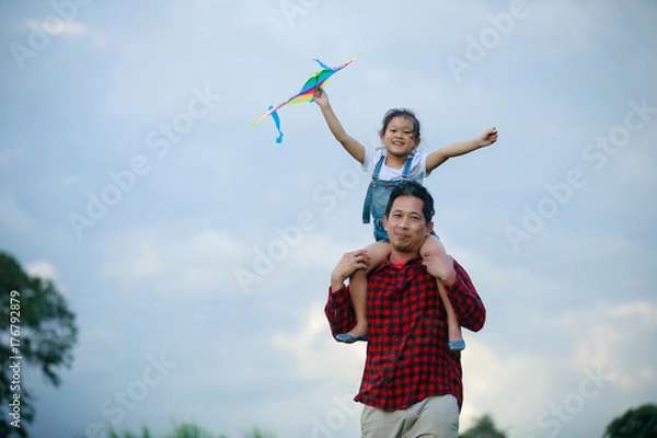 Fototapeta Asian child girl and father with a kite running and happy on meadow in summer in nature