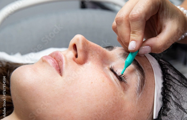 Obraz A client lies on a treatment table with their eyes closed during a lash lift procedure