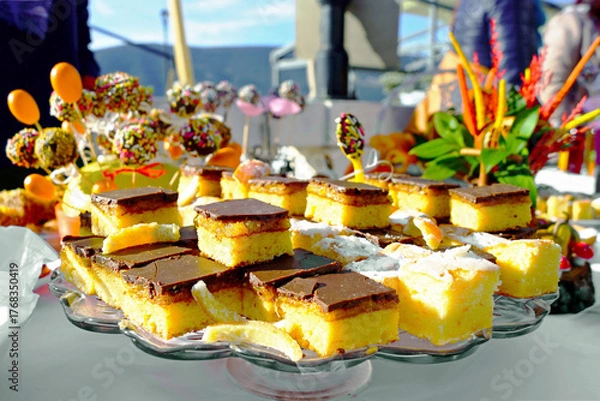 Obraz Sponge cake cut into squares with a layer of jam and chocolate icing at dessert buffet (Orange festival, Herceg Novi). Symbolizes festive confectionery display and community gathering sweet offering.