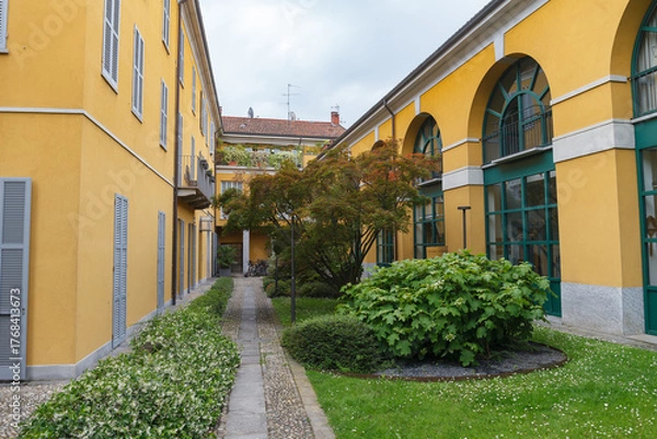 Fototapeta Greenery in the inner yard with pathwalks, historical stone bulding, yellow color, yearly XX century. Monza, Italy.