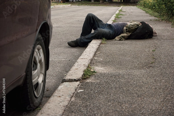 Fototapeta Pijany mężczyzna leżący na zewnątrz. Nieprzytomna osoba na ulicy. Bieda i alkoholizm.